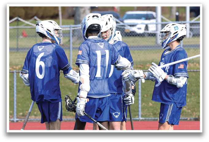 A group of young men wearing blue shirts and white socks are standing on a field holding lacrosse sticks. AI generated content