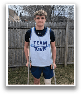 A young man wearing a white jersey with the words “Team MVP" on it stands on a wooden deck. He has a cast on one leg and is holding crutches for support. AI generated content