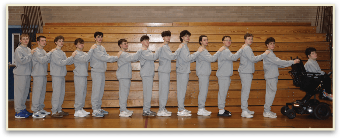 A group of young men are standing in a gym, wearing grey sweatshirts and white shoes. They are lined up in a row, with some of them holding hands with their neighbors. AI generated content