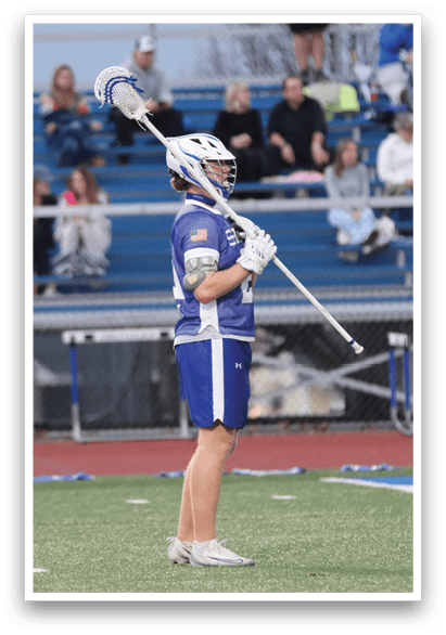 A lacrosse player wearing a blue uniform stands on a field holding a lacrosse stick. AI generated content