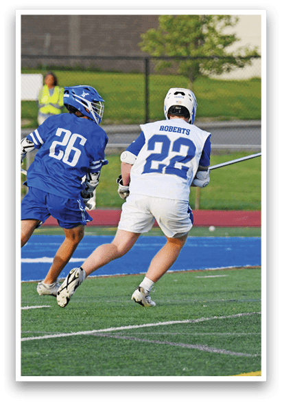 Two men playing lacrosse on a field. Description generated by AI