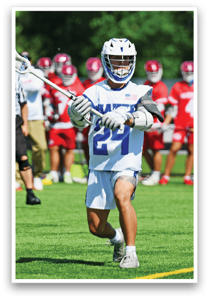 A man in a blue and white uniform holding a lacrosse stick. Description generated by AI
