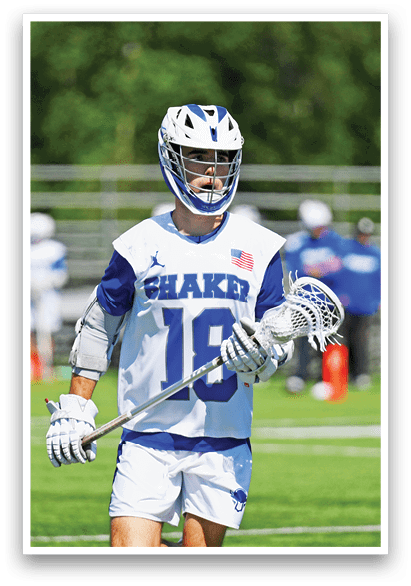 A man wearing a white and blue shirt and white shorts holding a lacrosse stick. Description generated by AI