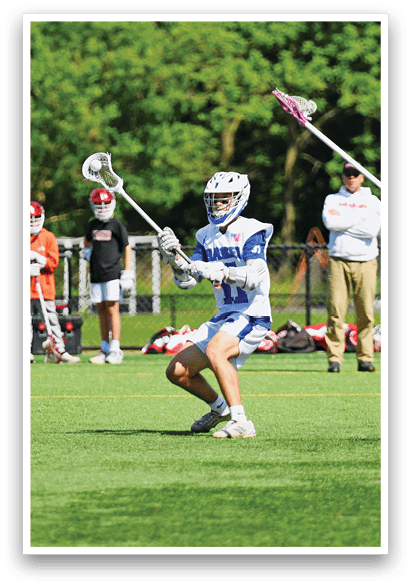 A man in a blue shirt and red shorts is running with a lacrosse stick. Description generated by AI