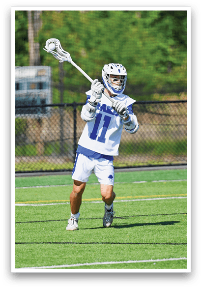 A man wearing a white and blue uniform holding a lacrosse stick. Description generated by AI