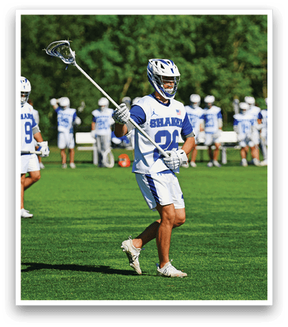 A man wearing a blue and white jersey is holding a lacrosse stick. Description generated by AI