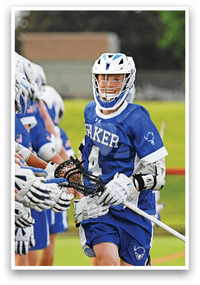 A man in a blue and white uniform is holding a lacrosse stick. Description generated by AI