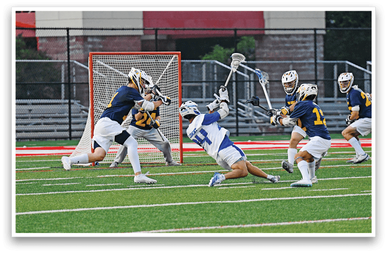 Five people in sports uniforms are actively playing lacrosse on a field near a goal net. Description generated by AI