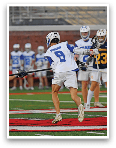 A person wearing a helmet and sports gear is playing lacrosse on a field while holding a lacrosse stick and facing another player. Description generated by AI