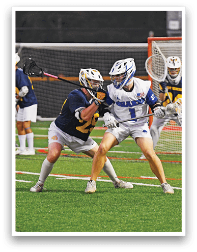 People wearing helmets and sports uniforms are playing lacrosse on a field with a goal in the background. Description generated by AI