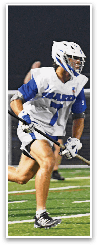 People wearing helmets and sports uniforms are playing lacrosse on a field at night. Description generated by AI