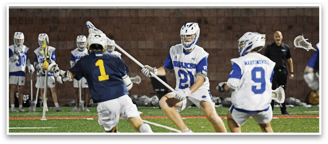 A person wearing a navy blue jersey with the number one is playing lacrosse on a field while other players in white and blue uniforms stand in the background. Description generated by AI