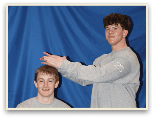 Two young men in grey sweatsuits are posing for a picture. One of them is holding his hand up to his face. AI generated content