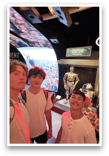 Three young men pose for a picture in front of a display featuring a statue of a knight and a robot. AI generated content