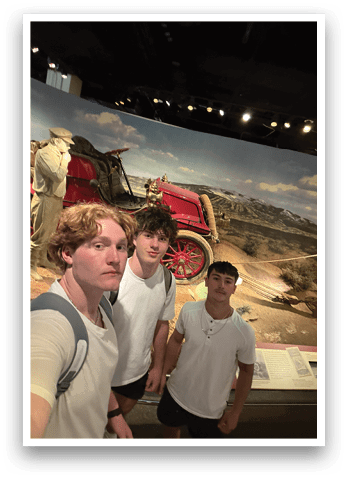 Three young men pose for a picture in front of a painting of a stagecoach. AI generated content