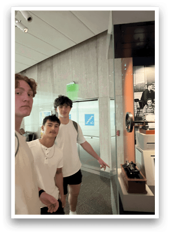 Three young men wearing white shirts and black shorts pose for a picture in front of a glass wall. AI generated content