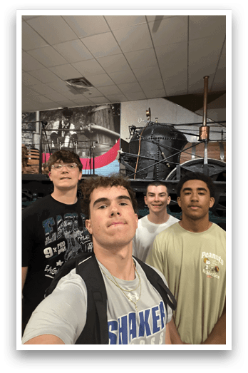 Four young men pose for a picture in front of a large machine. AI generated content