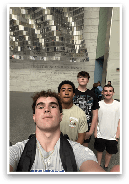 Four young men pose for a picture in front of a large metal sculpture. AI generated content