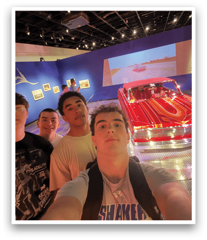 Four people pose in front of a red car in a museum. AI generated content