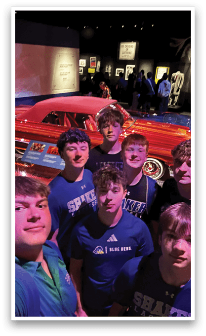 A group of young men pose for a picture in front of a red car. AI generated content