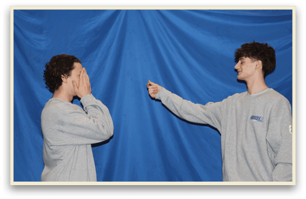 Two people standing in front of a blue curtain. One person is pointing at the other. AI generated content