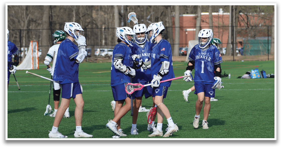 A group of lacrosse players wearing blue and white uniforms are standing on a field. They are holding their lacrosse sticks and talking to each other. There are several cars parked in the background. AI generated content