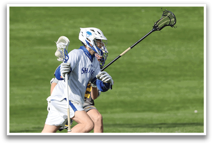 A man wearing a blue and white shirt and white shorts is playing lacrosse. Description generated by AI