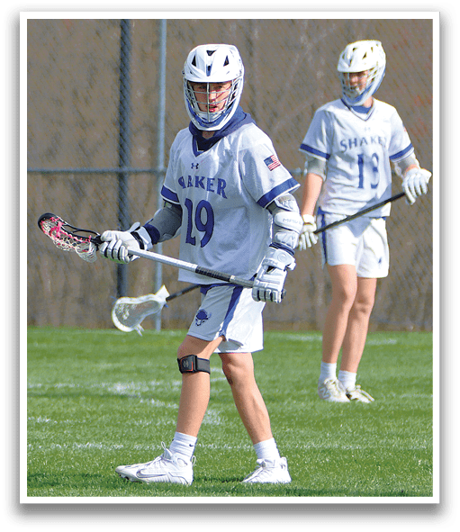 A man wearing a white and blue shirt and white shorts holding a lacrosse stick. Description generated by AI