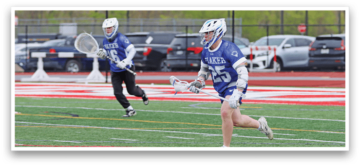 A man in a blue and white uniform is running on a field with a lacrosse stick. Description generated by AI