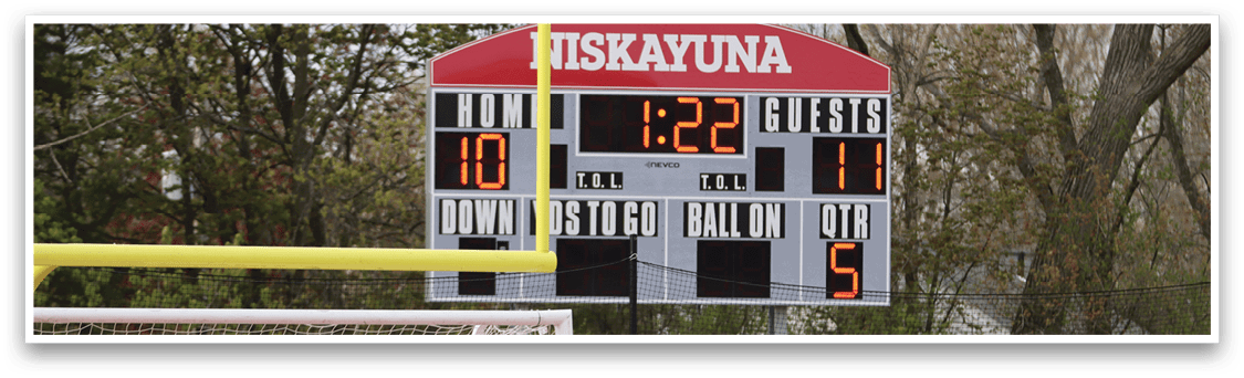 A soccer field with a scoreboard showing the time and score. Description generated by AI