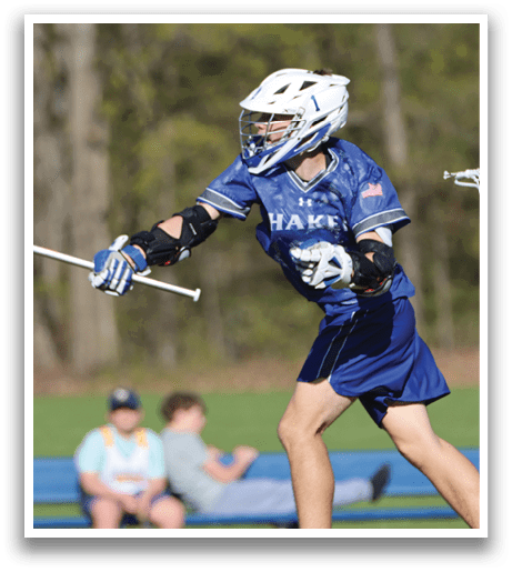 A boy in a blue and white uniform is playing lacrosse. Description generated by AI