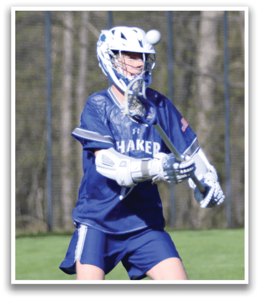 A boy wearing a blue shirt and shorts with a lacrosse stick. Description generated by AI