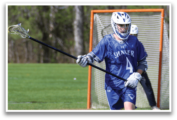 A young man wearing a blue and white jersey and holding a lacrosse stick. Description generated by AI