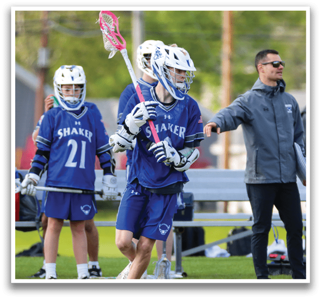A boy in a blue and white uniform holding a pink and white lacrosse stick. Description generated by AI