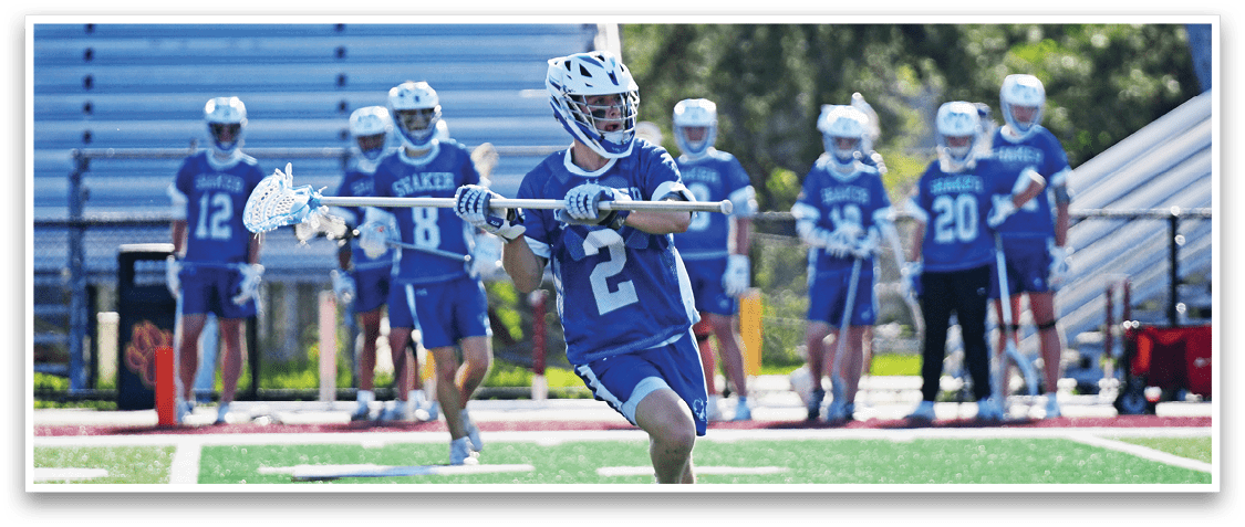 A man with a blue and white uniform is running with a stick in his hand. Description generated by AI