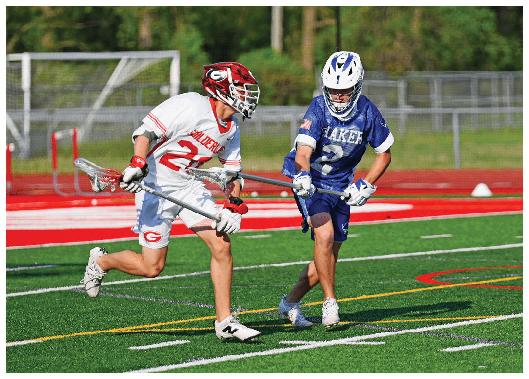 Two men playing lacrosse on a field. Description generated by AI