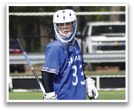 A young man wearing a blue and white jersey and holding a lacrosse stick. Description generated by AI