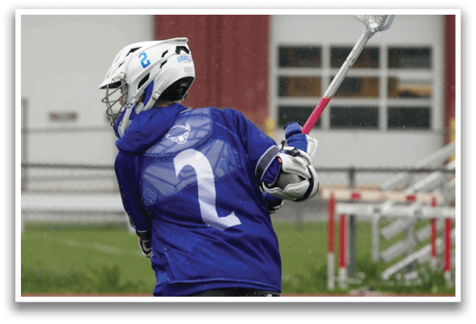 A man wearing a blue shirt and white pants is holding a lacrosse stick. Description generated by AI