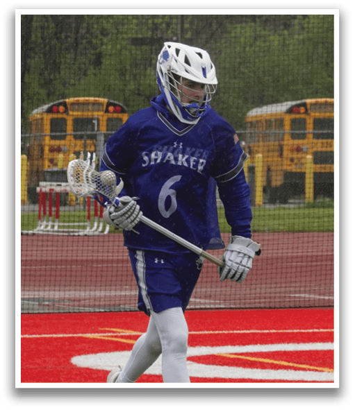 A man wearing a blue and white shirt and white pants is holding a lacrosse stick. Description generated by AI