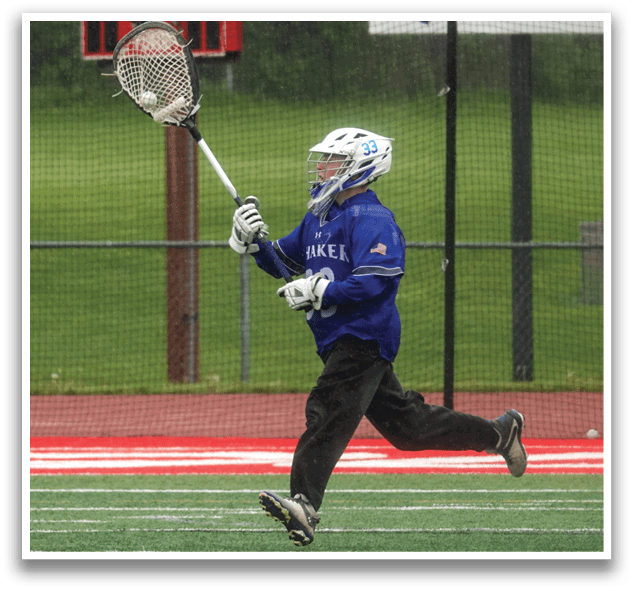 A person wearing a blue shirt and black pants is running with a lacrosse stick. Description generated by AI
