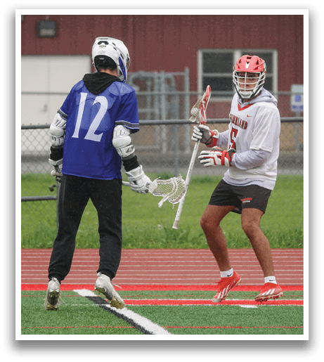 Two men playing lacrosse on a field. Description generated by AI