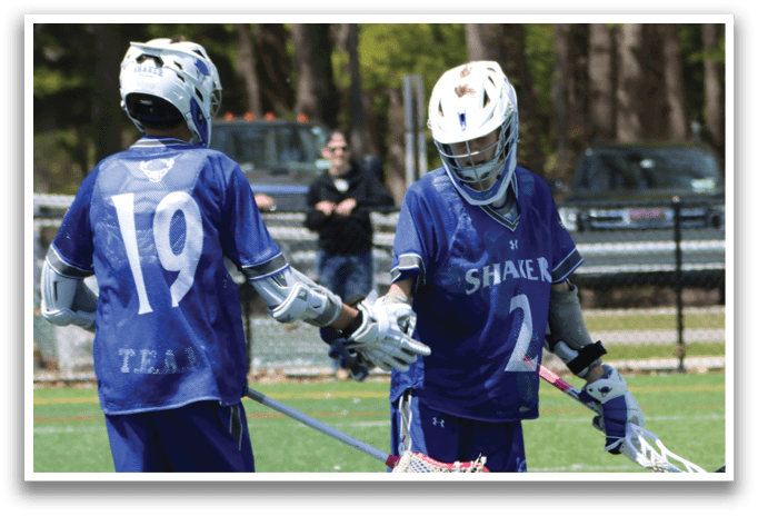 Two boys wearing blue and white uniforms are playing lacrosse. Description generated by AI