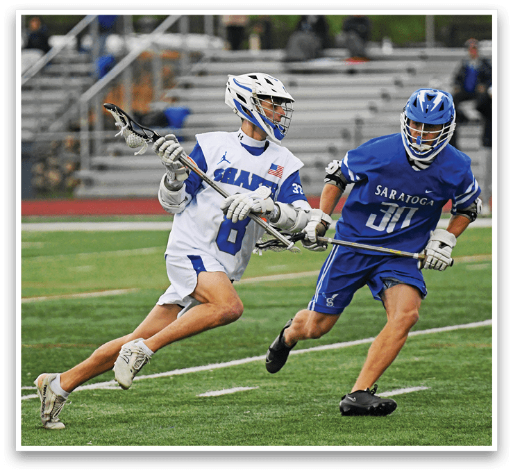 Two men playing lacrosse on a field. Description generated by AI