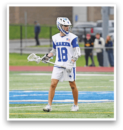 A man wearing a blue and white shirt and white shorts is holding a lacrosse stick. Description generated by AI