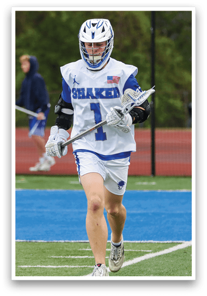 A man wearing a white and blue shirt and white shorts is holding a lacrosse stick. Description generated by AI
