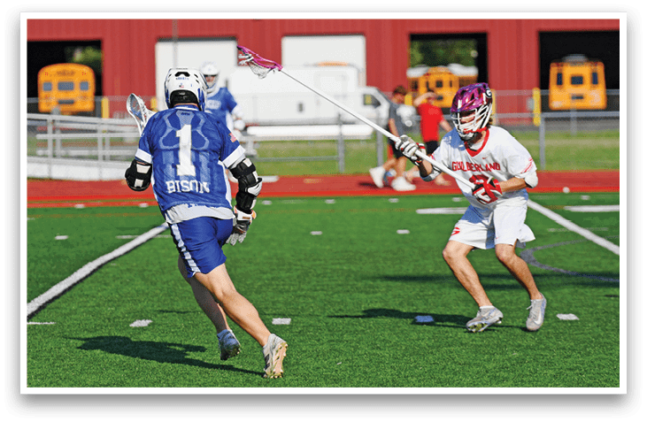 Two people playing lacrosse on a field. Description generated by AI