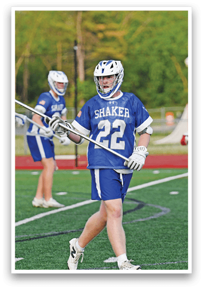 A man wearing a blue and white shirt and white shorts is holding a lacrosse stick. Description generated by AI