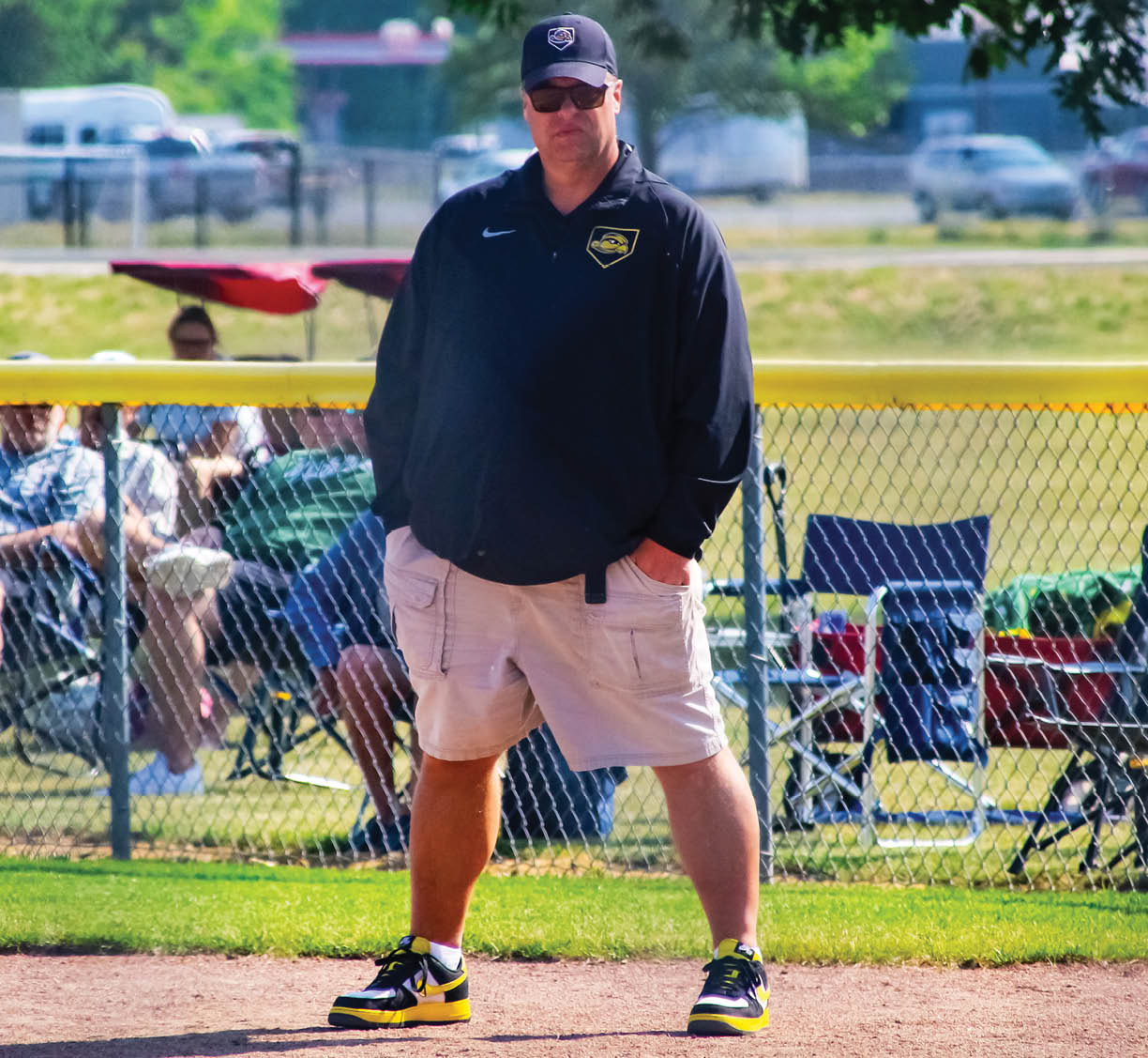 A man wearing a black jacket and a black hat standing on a baseball field. Description generated by AI