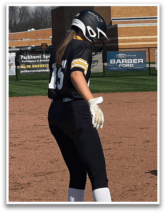 A female baseball player is standing on a base, wearing a black and yellow jersey. AI generated content