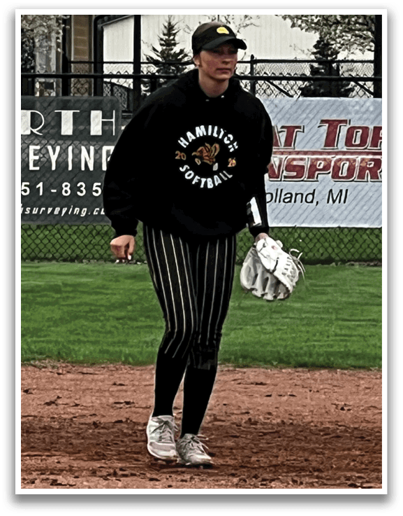 A woman wearing a black shirt and white pants stands on a baseball field. AI generated content